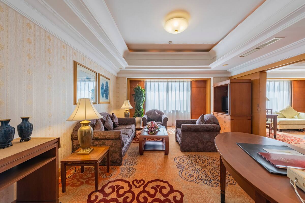 A spacious living room with a sofa set, a coffee table, and a TV. There are decorative vases and a plant on the side table.