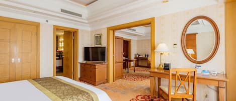 A hotel room with a large bed, a desk, a chair, a television, a mirror, and a carpeted floor.