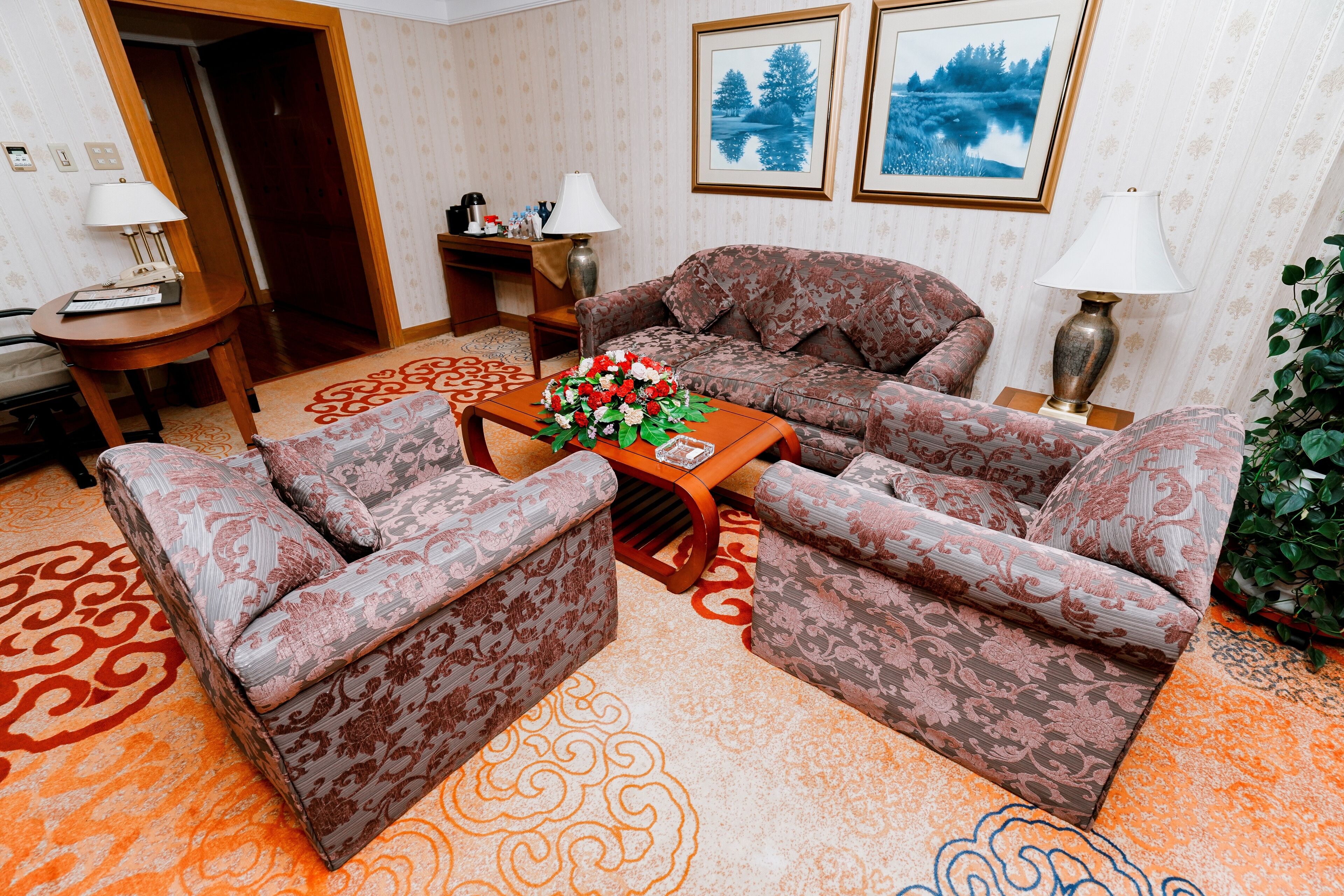 Un salón con sofás estampados, una mesa de centro con un arreglo floral y una alfombra de diseño geométrico.