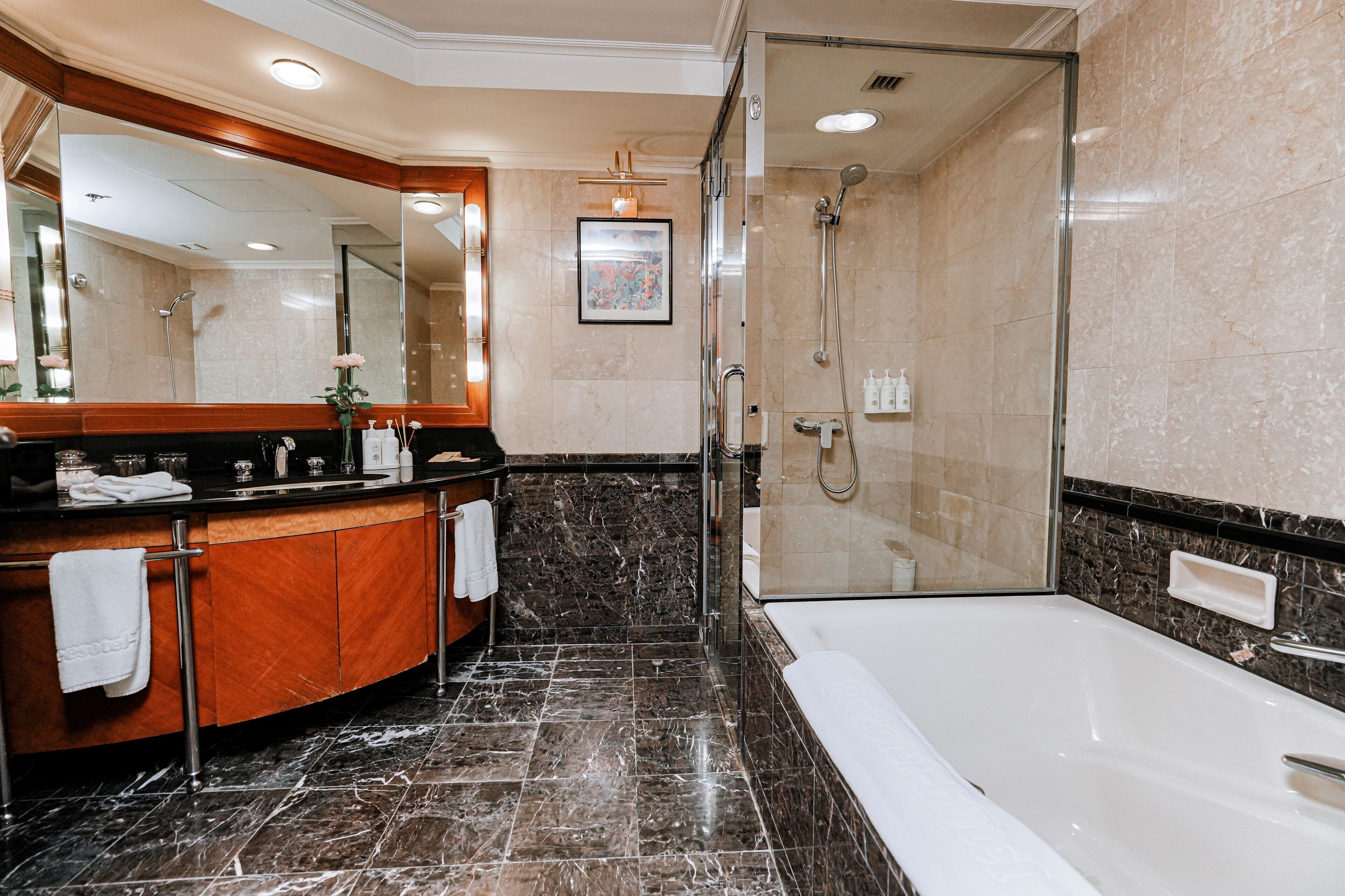 A modern bathroom with a marble floor, a large mirror, a bathtub, and a glass-enclosed shower area.