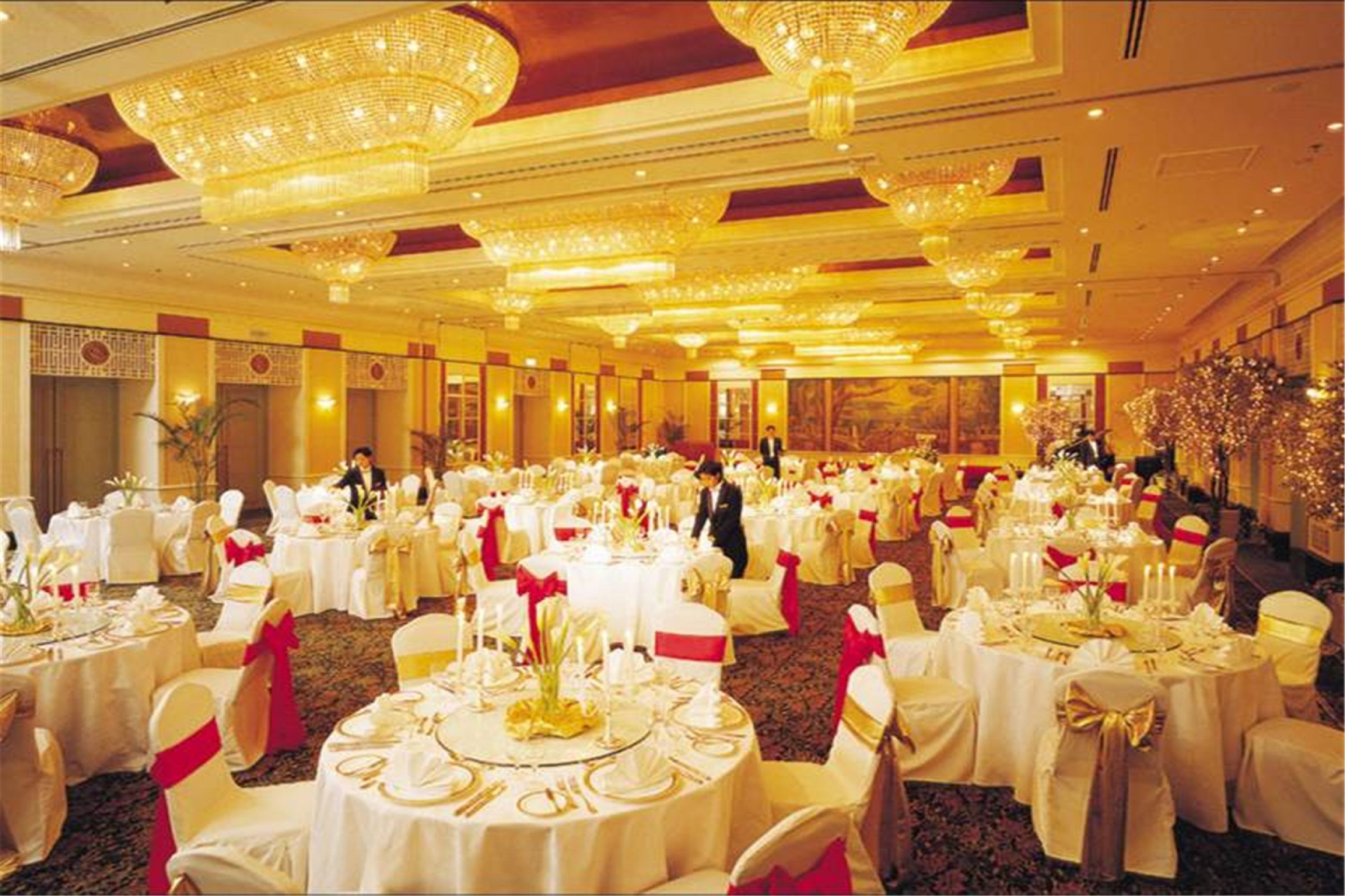 A banquet hall with round tables set for a formal event, featuring chandeliers and a carpeted floor.