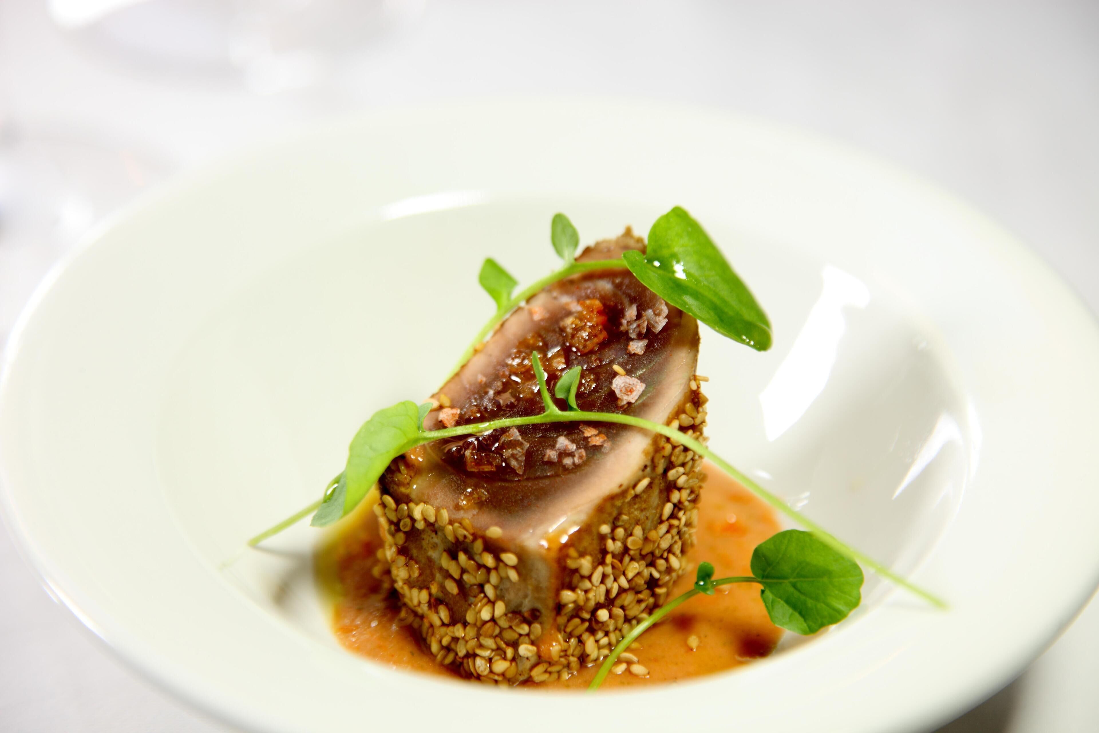 Un plato con un centro de carne, decorado con hojas verdes y semillas de sésamo.