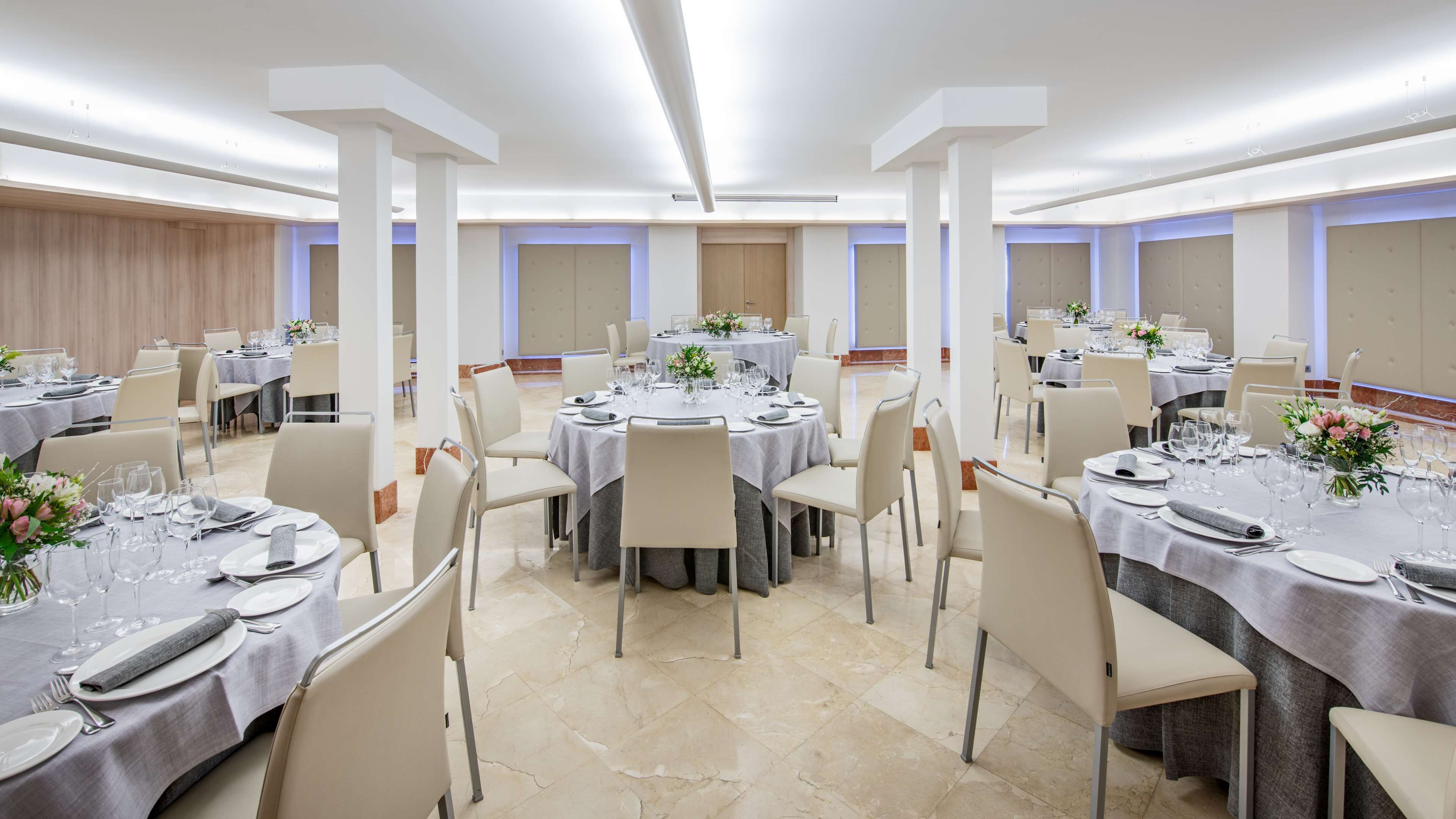 A banquet hall with round tables set for dining, featuring white tablecloths, chairs, and floral centerpieces.