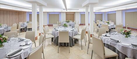 A banquet hall with round tables set for dining, featuring white tablecloths, chairs, and floral centerpieces.