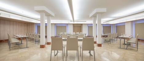 A spacious conference room with multiple tables and chairs, high ceilings, and modern lighting.