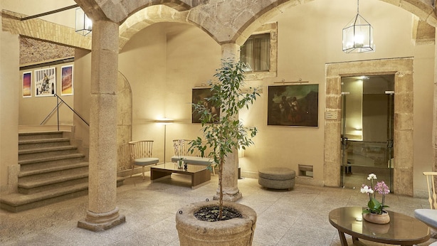 A spacious atrium with a central staircase, stone columns, and a seating area with a potted plant. - NH Collection Cáceres Palacio de Oquendo (Cáceres)