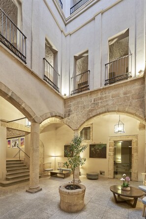 A spacious atrium with a central staircase, stone columns, and a seating area with a potted plant.