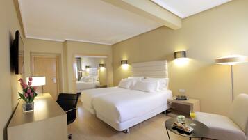 Habitación de hotel con una cama grande, un escritorio, una silla, una mesita con una bebida y una lámpara.