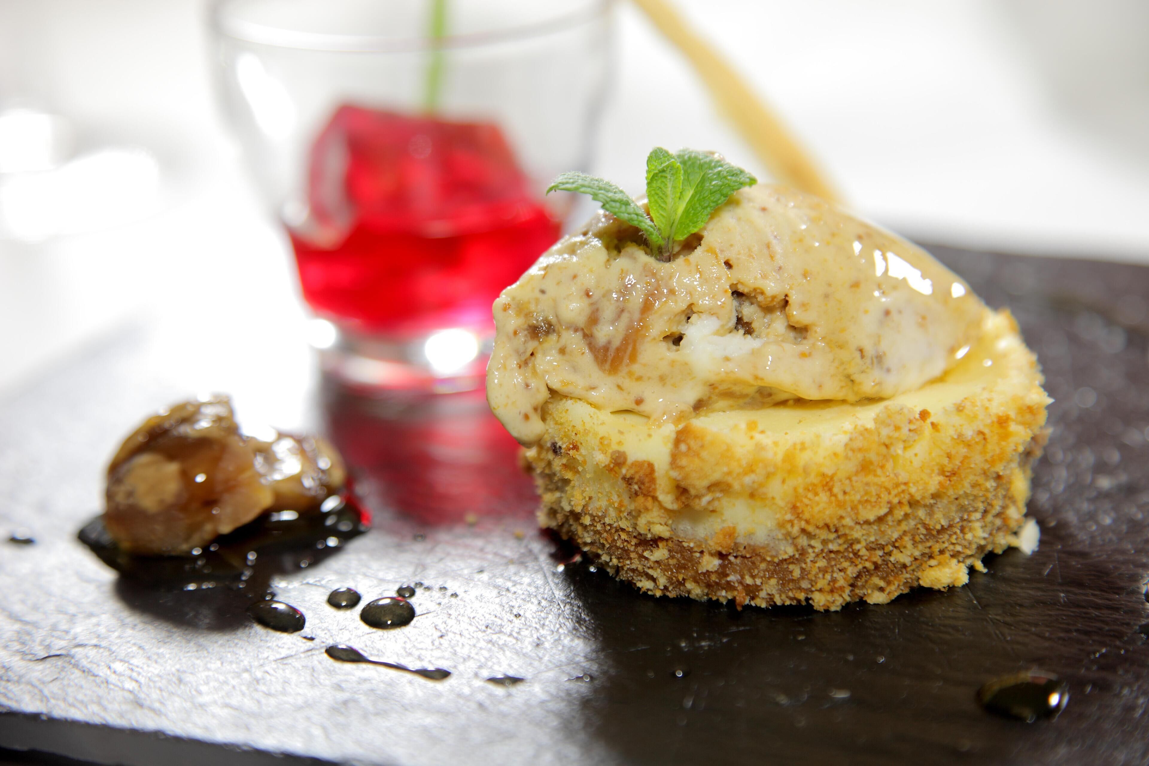 Un dessert composé d’une base friable et d’une garniture crémeuse, accompagné d’un petit morceau de chocolat et d’un verre contenant un liquide rouge.