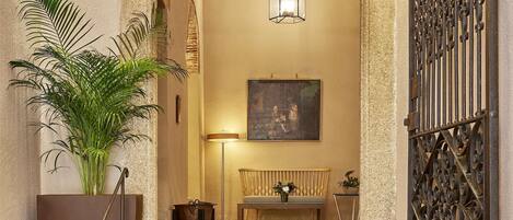 A stone staircase leading to a lobby with a wrought iron gate, a bench, a potted plant, and a wall-mounted light fixture.