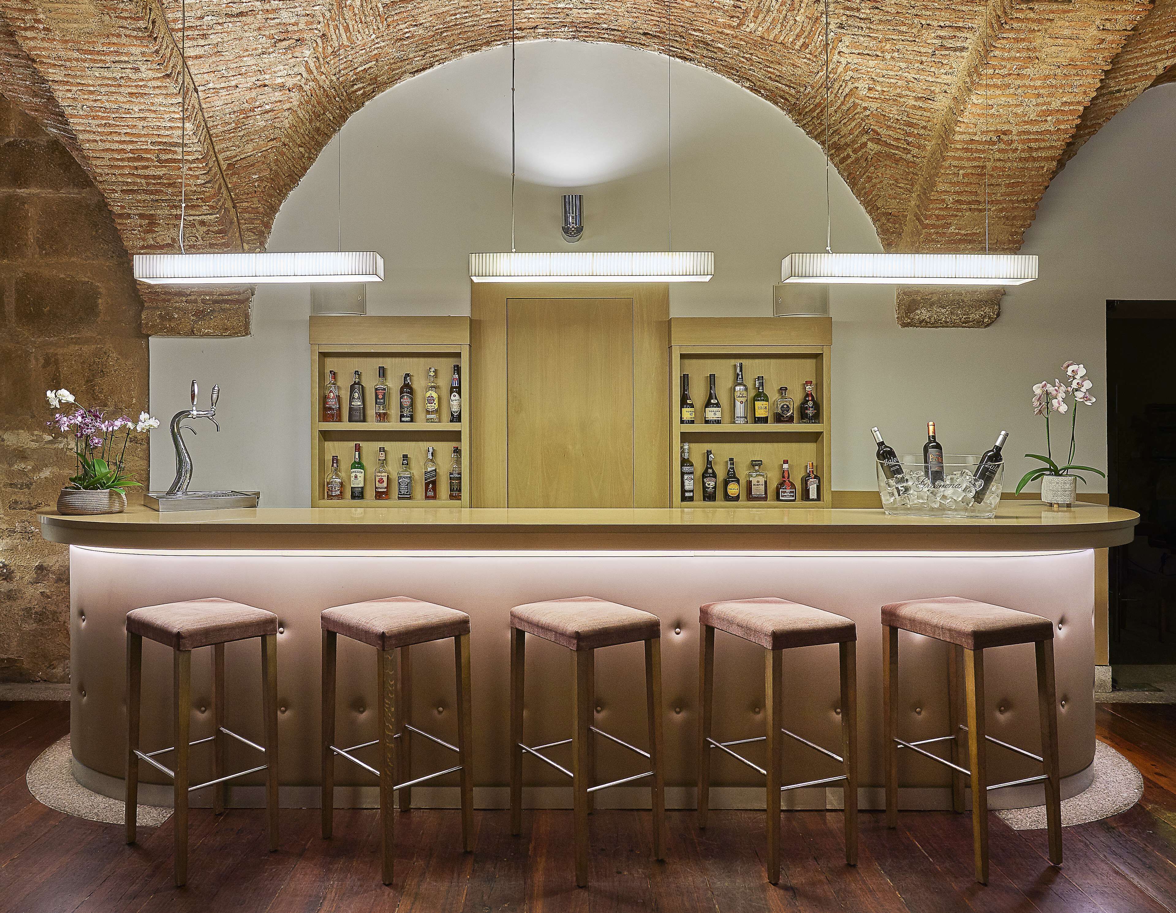 Zona de bar con mostrador de madera, varios taburetes y estantes llenos de botellas de licores.