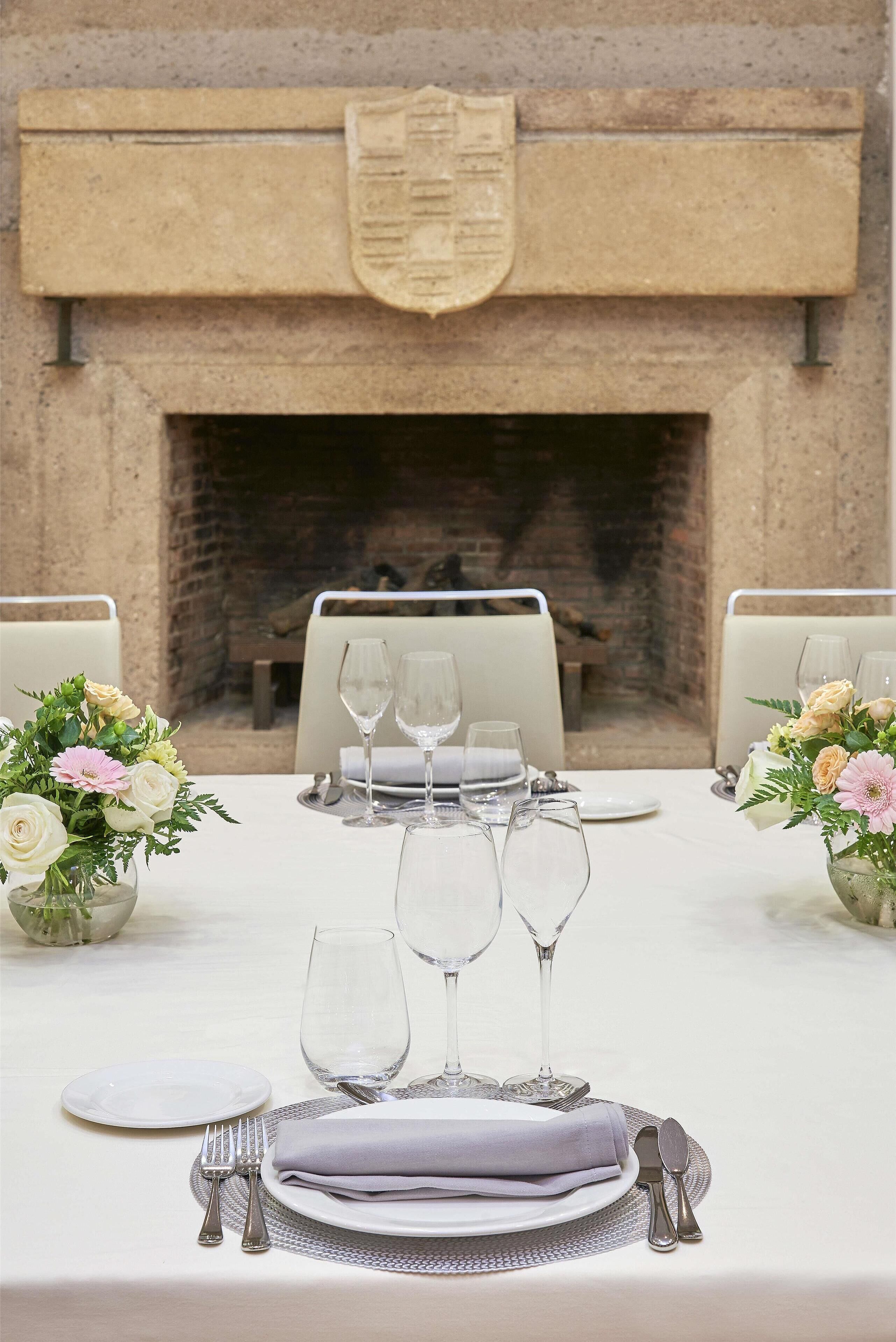 Une table à manger dressée pour deux personnes, avec une nappe blanche, des couverts en argent et de la verrerie, agrémentée de compositions florales de chaque côté.