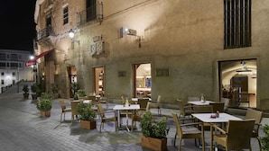 An outdoor cafe area with tables and chairs, potted plants, and a building with a sign that reads "The Collection Hotel". - NH Collection Cáceres Palacio de Oquendo (Cáceres)