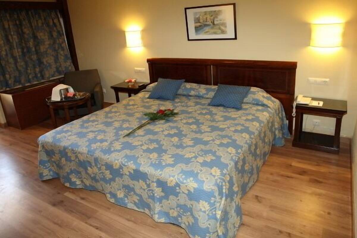 Una cama bien tendida con ropa de cama floral, dos lámparas de noche y un cuadro en la pared.