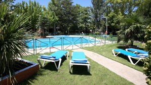 A pool area with a fenced pool, surrounded by grass and trees. There are lounge chairs along the poolside. - Hotel El Hidalgo (Valdepenas)
