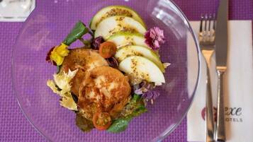A clear glass bowl containing a salad with sliced apples, lettuce, and a piece of bread, placed on a purple tablecloth.