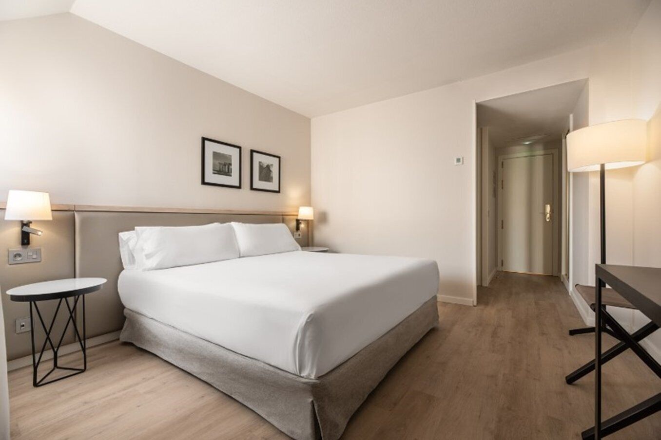 Una habitación de hotel con una cama, mesitas de noche, un escritorio y una lámpara.