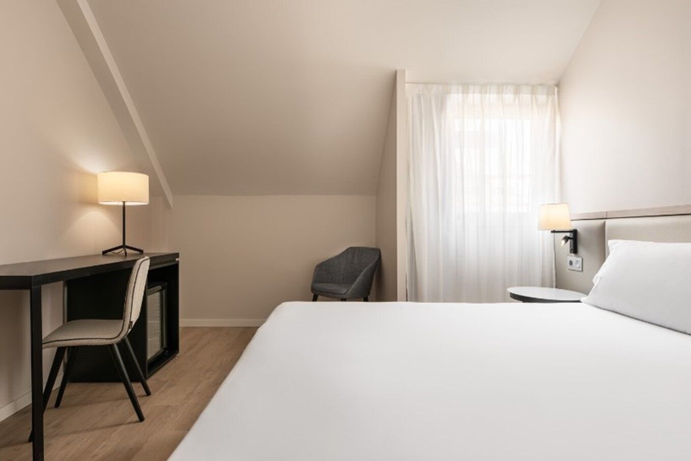 Habitación de hotel con cama, escritorio, silla y dos lámparas de noche.