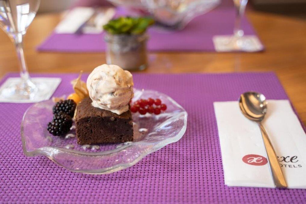 A dessert plate with a scoop of ice cream, a piece of cake, and berries on a purple placemat.