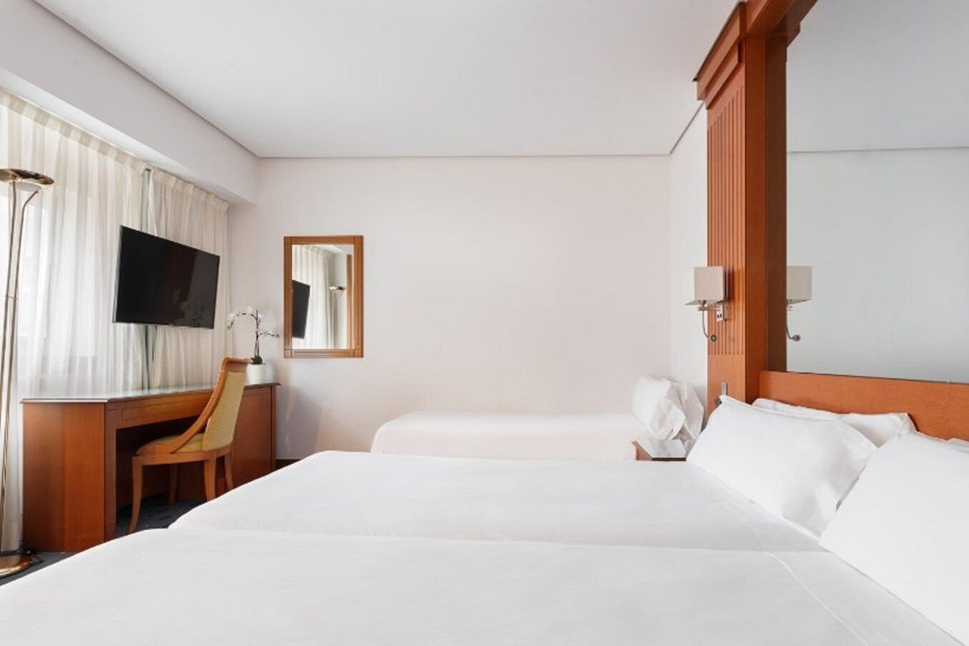 A hotel room with two beds, a desk, a chair, a TV, and a mirror.