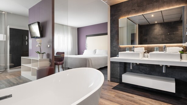 A modern bathroom with a freestanding bathtub, a large mirror, and a vanity with two sinks. - Exe Coruña (A Coruña)