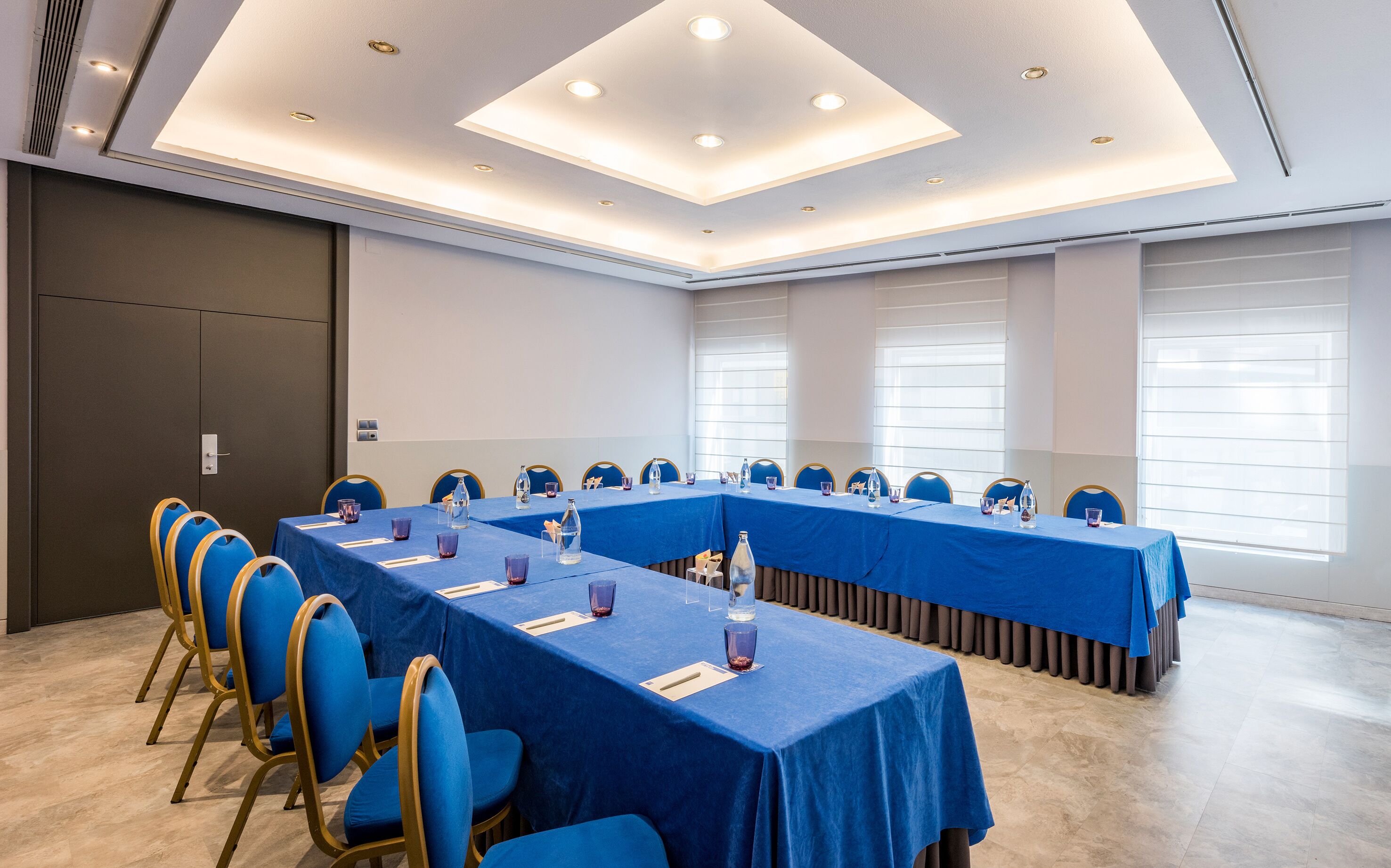 A conference room with long tables, blue chairs, and a modern ceiling design.