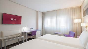 A hotel room with two beds, a desk, a chair, a TV, and a window with curtains.