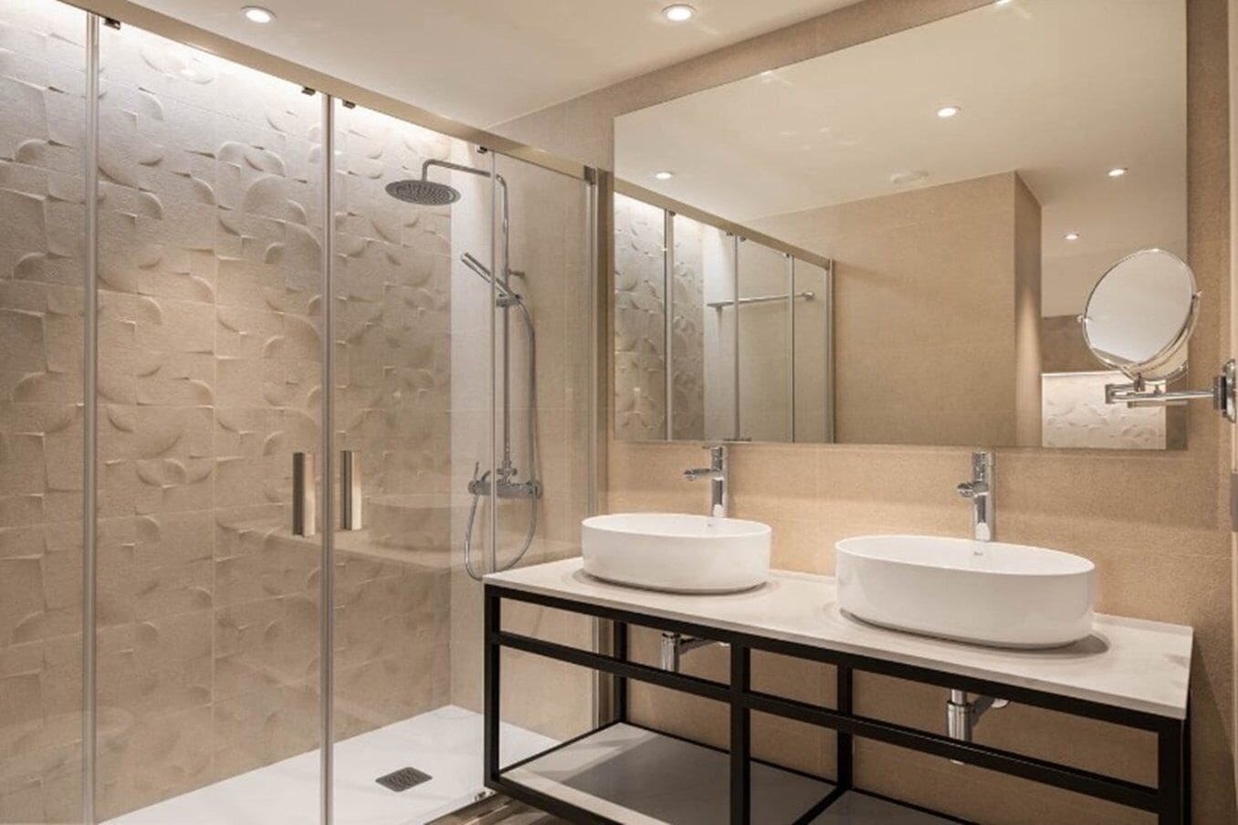 A modern bathroom with two round sinks, a glass shower enclosure, and a large mirror.