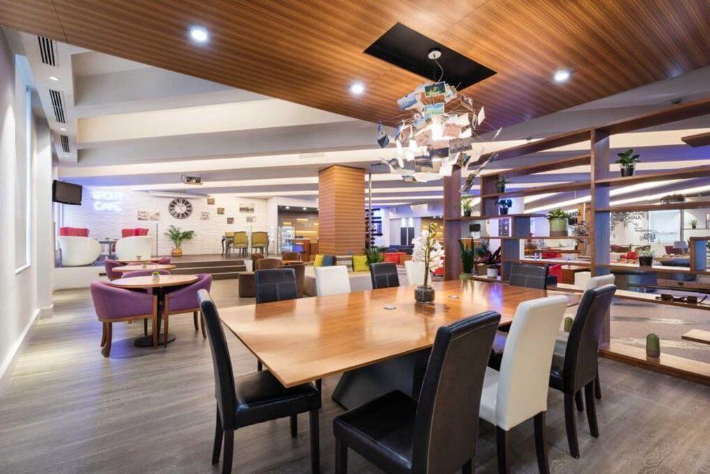 A modern dining area with a wooden table and chairs, surrounded by shelves with plants and decorative items.
