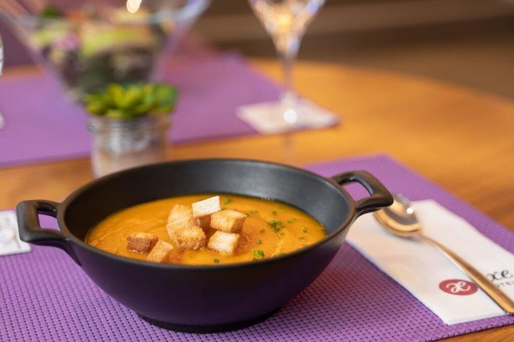 A bowl of soup with croutons on a purple mat.