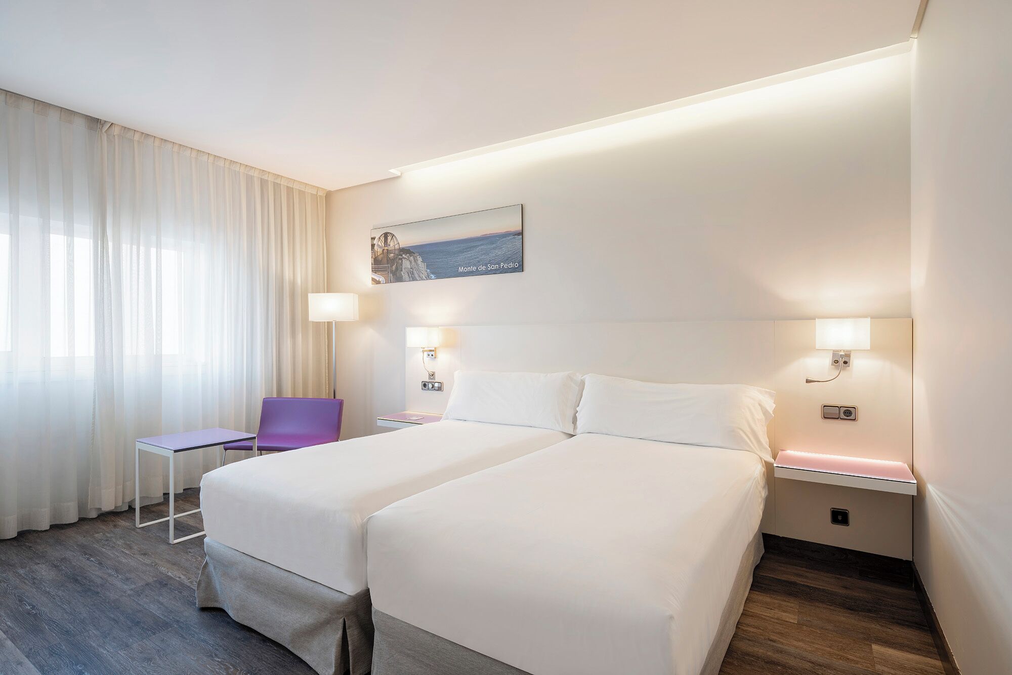 Habitación de hotel con dos camas, un escritorio, una silla y un cuadro en la pared.