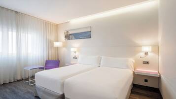 Habitación de hotel con dos camas, un escritorio, una silla y un cuadro en la pared.