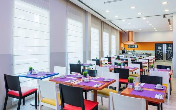 A modern restaurant with multiple dining tables and chairs, large windows, and a kitchen area. - Exe Coruña (A Coruña)