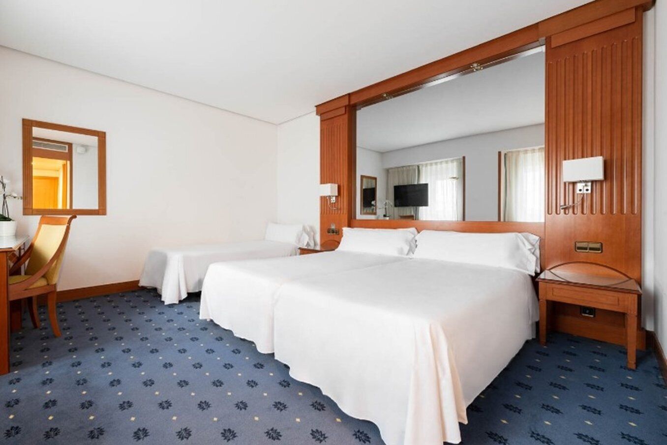 Habitació d'hotel amb dos llits, un escriptori, una cadira, un mirall i una televisió.