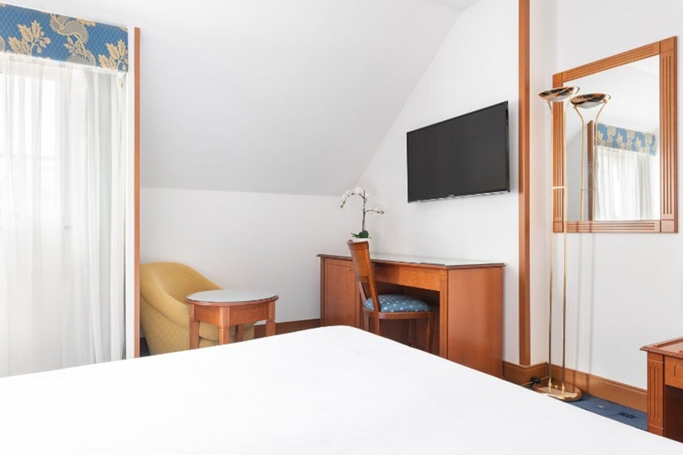 Une chambre d’hôtel équipée d’un lit, d’un bureau, d’une chaise, d’une télévision et d’un miroir.