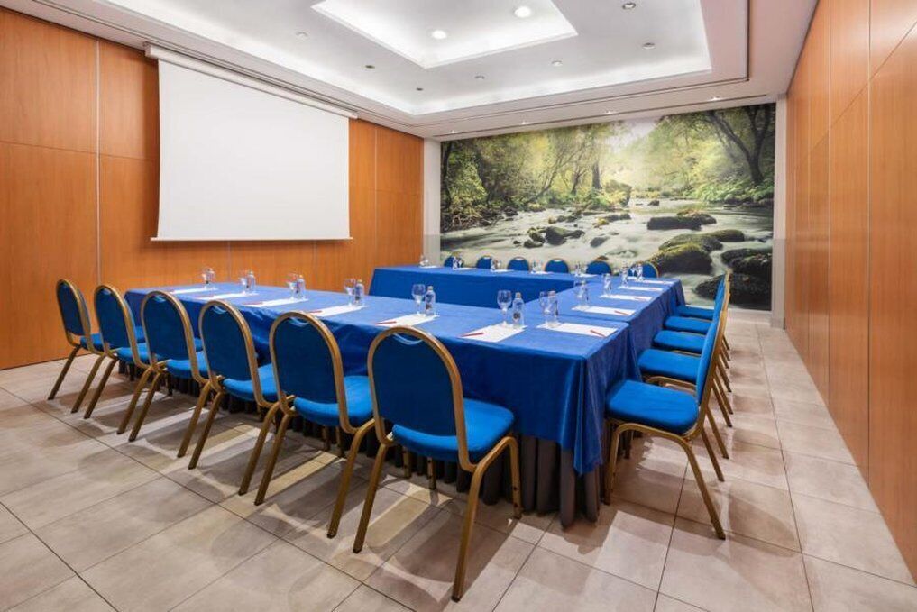 A conference room with a long table, blue chairs, a projector screen, and a scenic wall mural.
