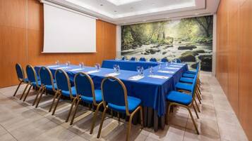 A conference room with a long table, blue chairs, a projector screen, and a scenic wall mural.