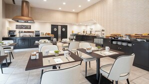 A modern dining area with multiple tables, chairs, and a kitchen area with breakfast items. - Exe Coruña (A Coruña)