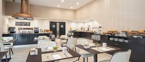 A modern dining area with multiple tables, chairs, and a kitchen area with breakfast items.