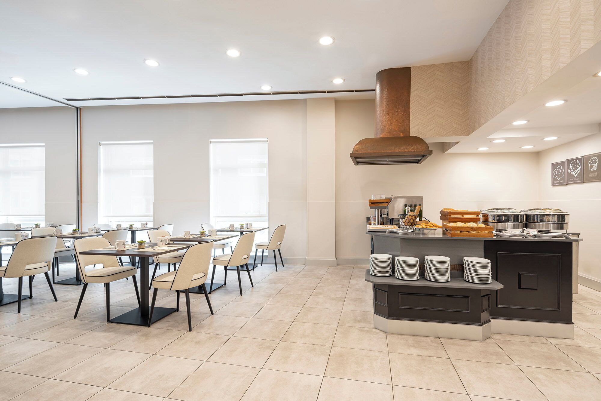 A modern dining area with tables and chairs, a kitchen counter with food items, and a large window providing natural light.
