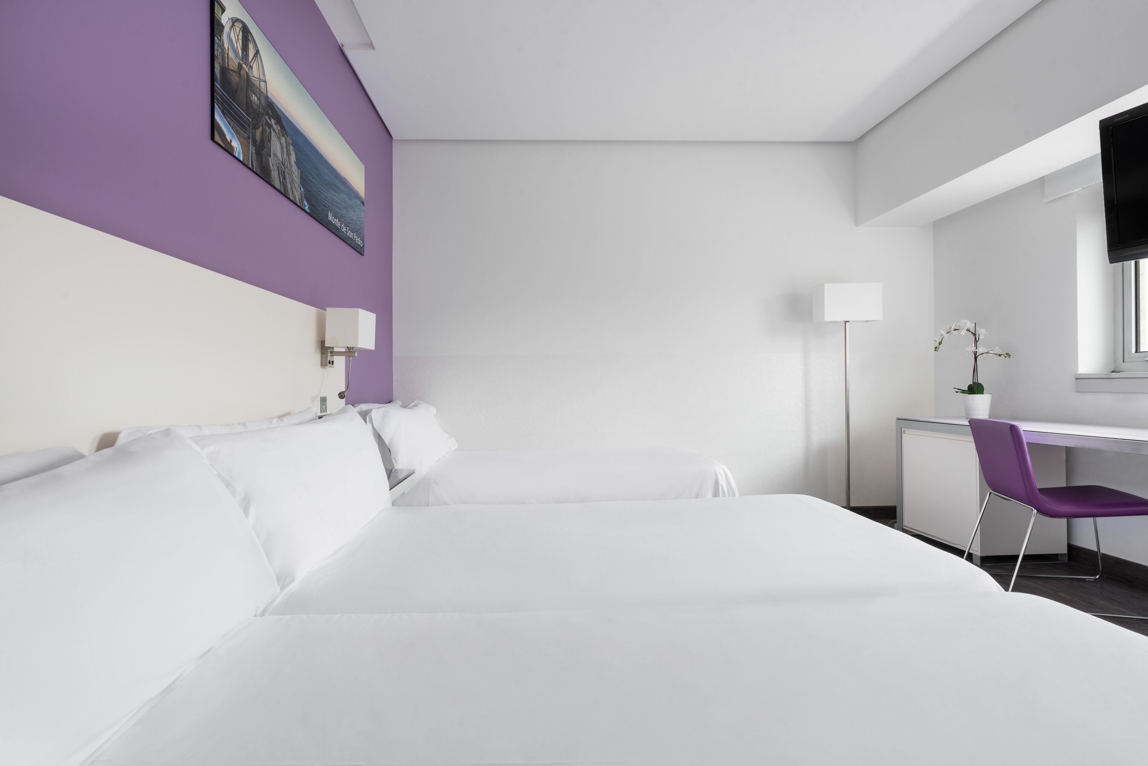 A modern hotel room with a large bed, a desk with a chair, a flat-screen TV, and a painting on the wall.