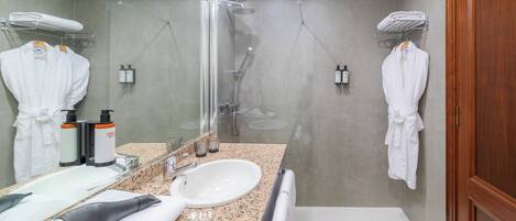 Un baño con lavamanos, espejo, perchas para bata y ducha.