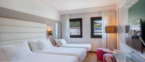 Habitación de hotel con dos camas, televisión, escritorio y vistas a edificios.