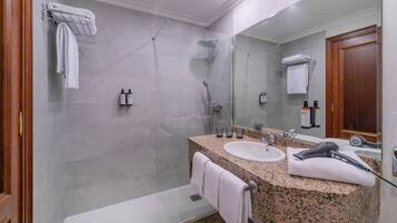 A modern bathroom with a granite countertop, a white sink, a hairdryer, and a glass-enclosed shower.