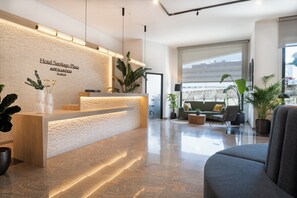 Welcome to Hotel Santiago Plaza, where guests can check in and relax in a clean, minimalist reception area with a seating area and potted plants.