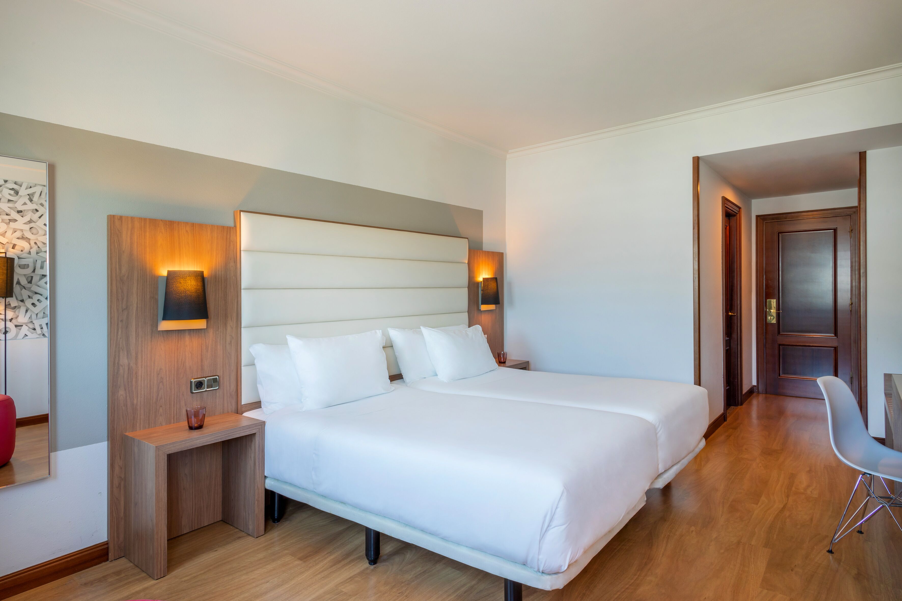 A hotel room with a large bed, two bedside tables, a chair, and a wooden headboard.