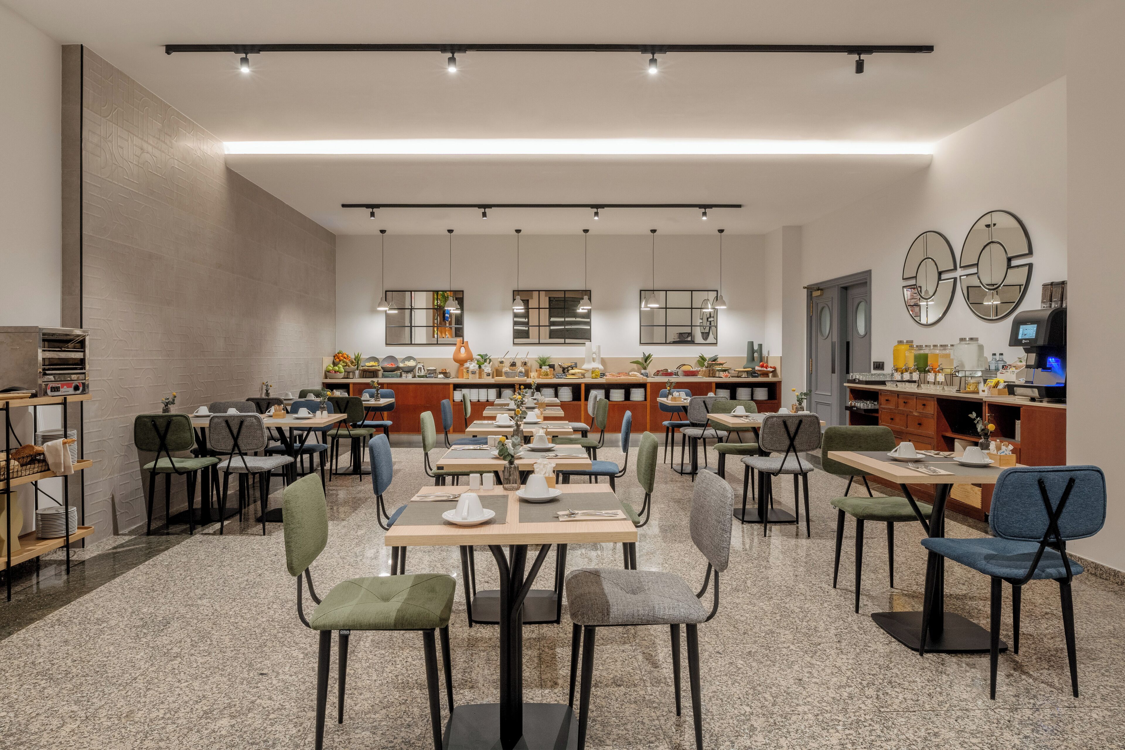 Een moderne eethoek met meerdere tafels en stoelen, een keuken op de achtergrond en een schone, goed verlichte ruimte.