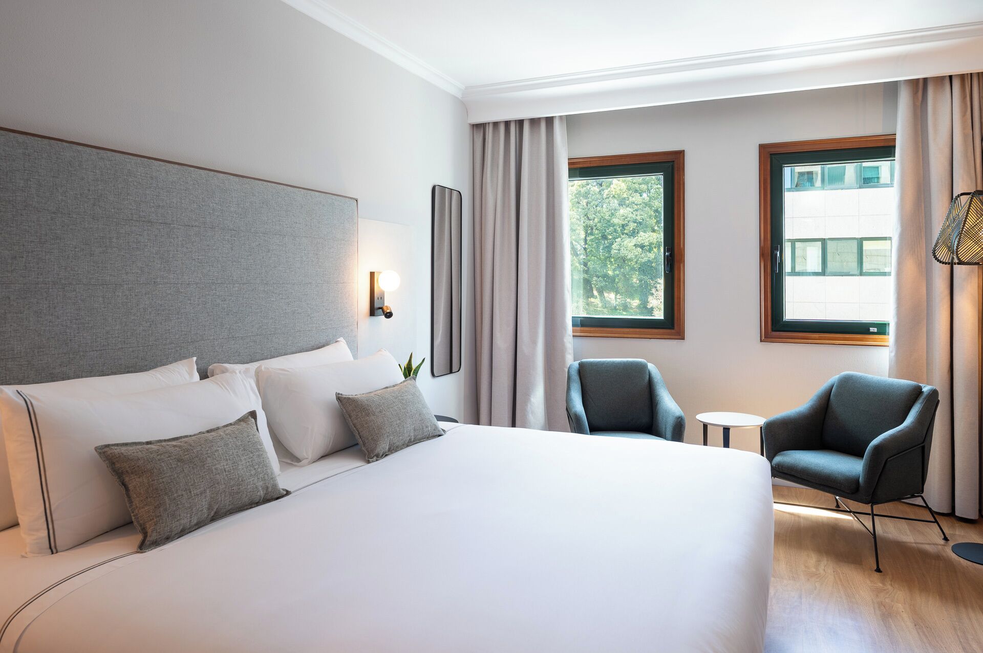 Ein Hotelzimmer mit einem großen Bett, zwei Sesseln, einem kleinen Tisch und einem Fenster mit Vorhängen.
