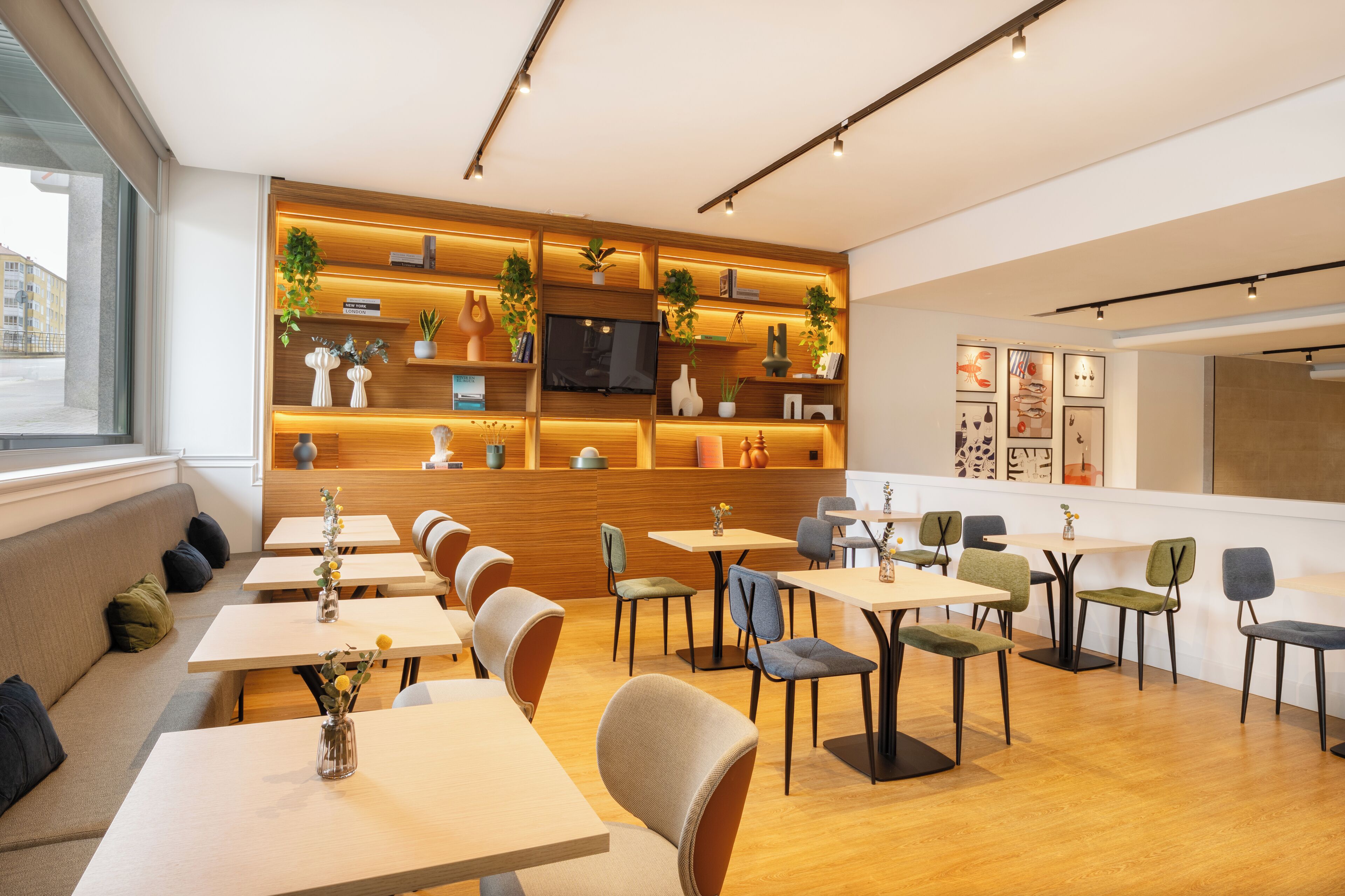A modern cafe with wooden shelves, comfortable seating, and a TV screen.