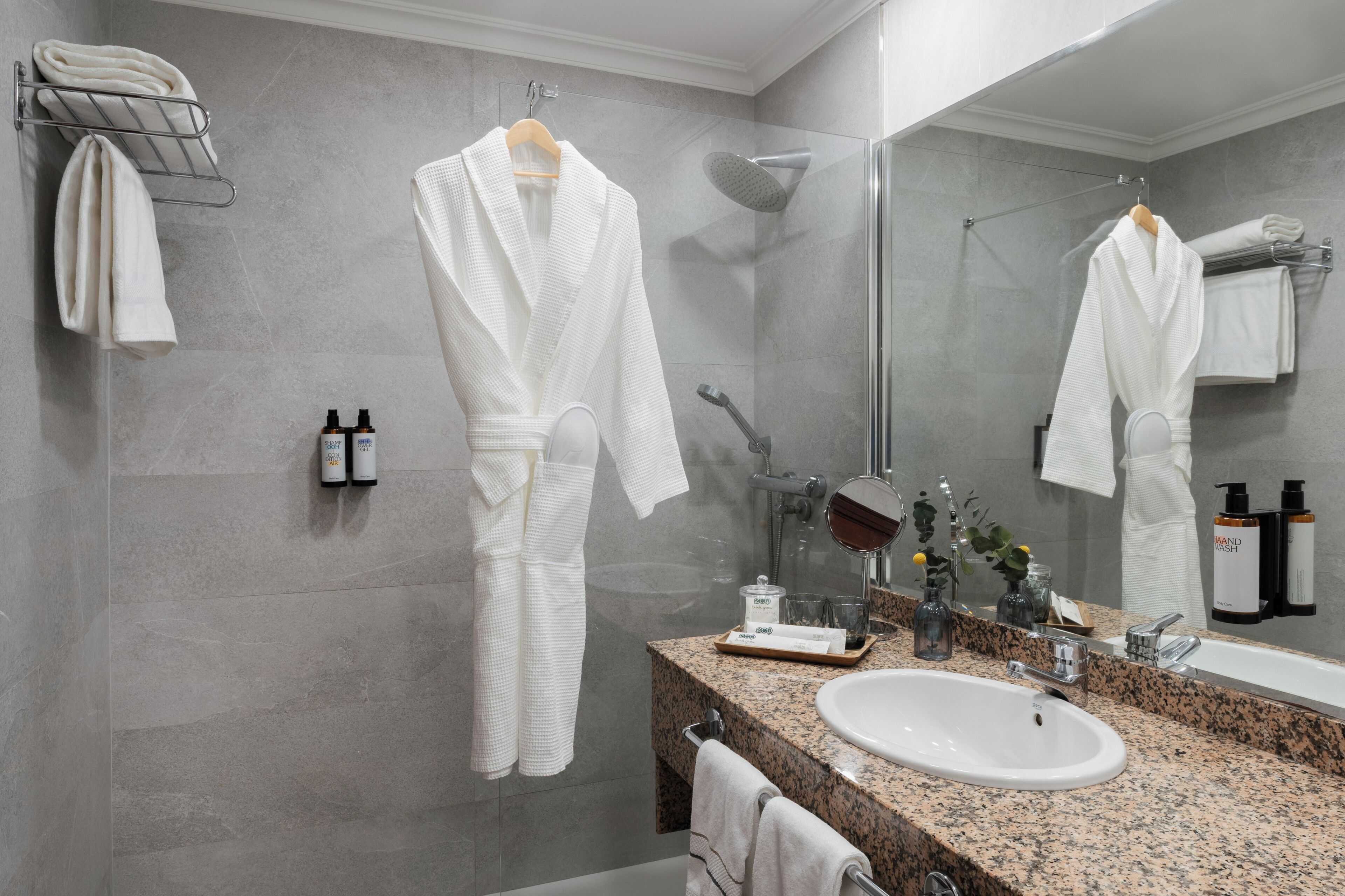 Ein modernes Badezimmer mit einer Granittheke, einem weißen Waschbecken, einer Duschkabine aus Glas und einem großen Spiegel.